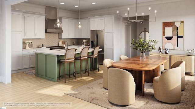 kitchen featuring wall chimney exhaust hood, a kitchen island with sink, light countertops, stainless steel fridge, and decorative backsplash