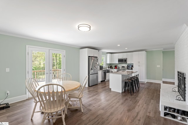 dining room with crown molding, baseboards, a brick fireplace, and dark wood finished floors