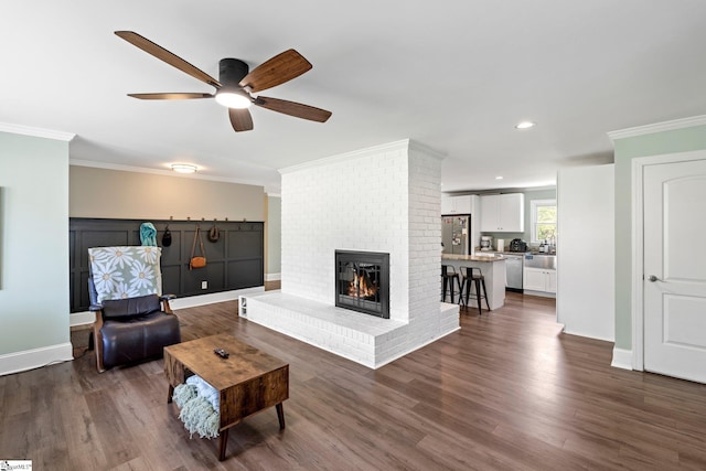 living room featuring baseboards, ornamental molding, dark wood-style floors, a ceiling fan, and a brick fireplace