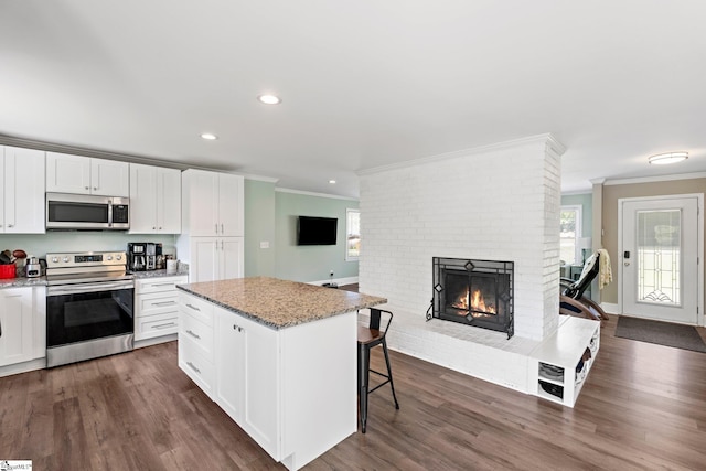 kitchen featuring a center island, crown molding, light stone countertops, a brick fireplace, and appliances with stainless steel finishes