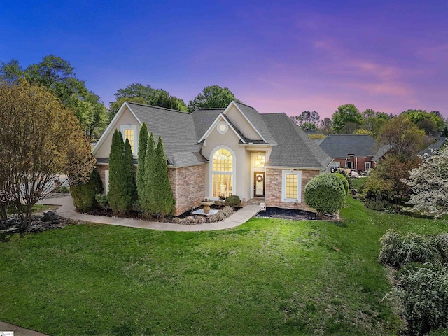 view of front of property featuring a front yard, stucco siding, stone siding, and roof with shingles