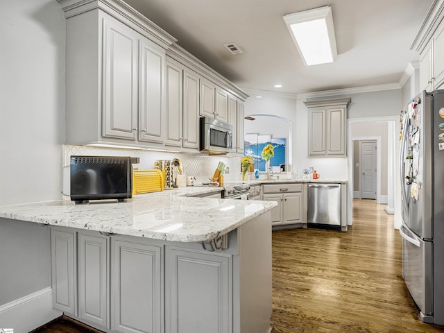 kitchen featuring light stone counters, a peninsula, dark wood finished floors, stainless steel appliances, and decorative backsplash