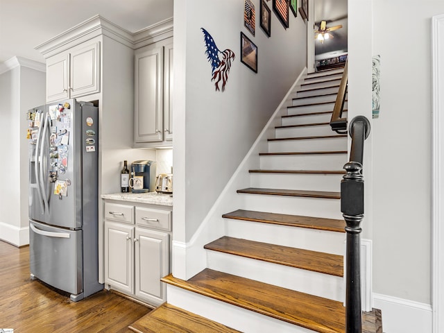 staircase with wood finished floors, ceiling fan, and baseboards