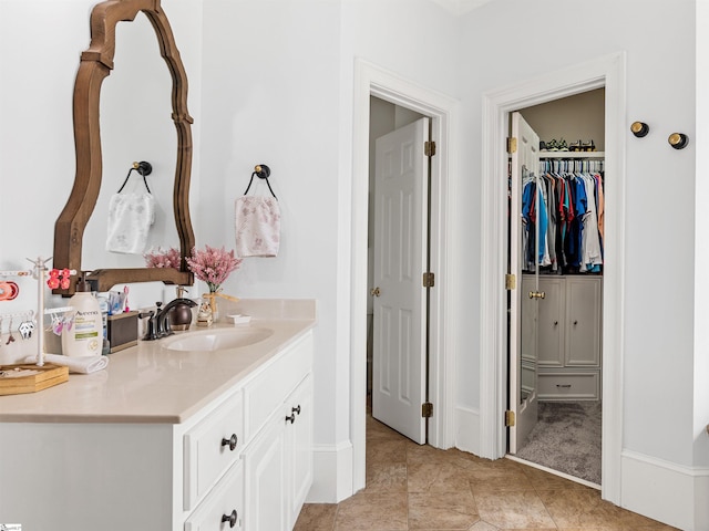 bathroom with tile patterned floors, a walk in closet, vanity, and baseboards