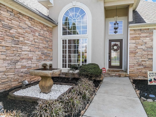 doorway to property featuring roof with shingles, stucco siding, and stone siding