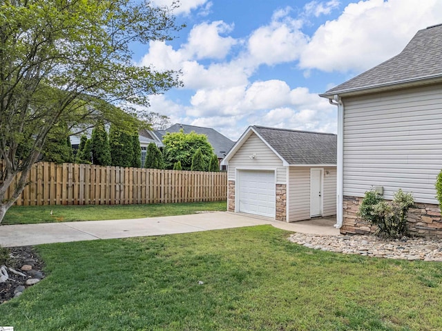 view of yard featuring an attached garage, an outbuilding, driveway, and fence