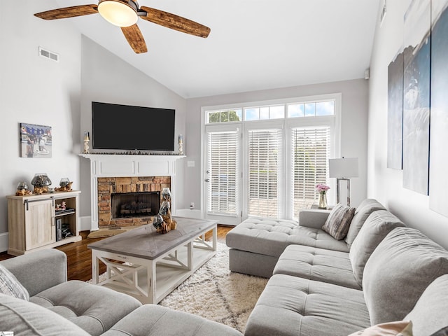 living room with ceiling fan, a stone fireplace, visible vents, wood finished floors, and baseboards