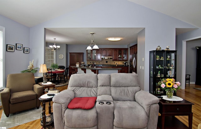 living room featuring light wood-style floors, a notable chandelier, a healthy amount of sunlight, and lofted ceiling