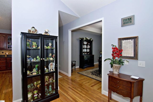 hall featuring light wood-style flooring and vaulted ceiling