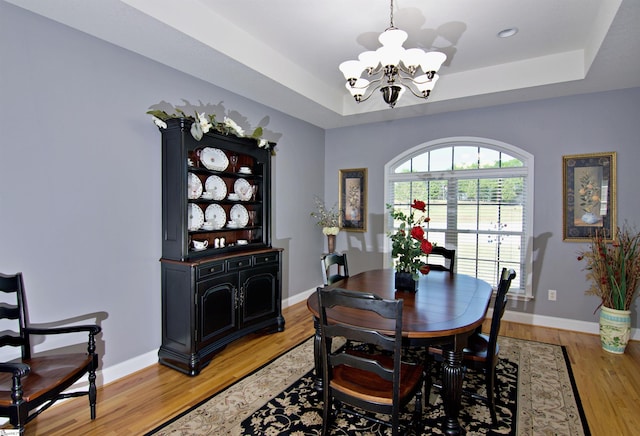 dining area with light wood-style floors, a notable chandelier, a tray ceiling, and baseboards