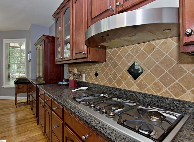 kitchen featuring glass insert cabinets, light wood-style flooring, ventilation hood, stainless steel gas cooktop, and decorative backsplash
