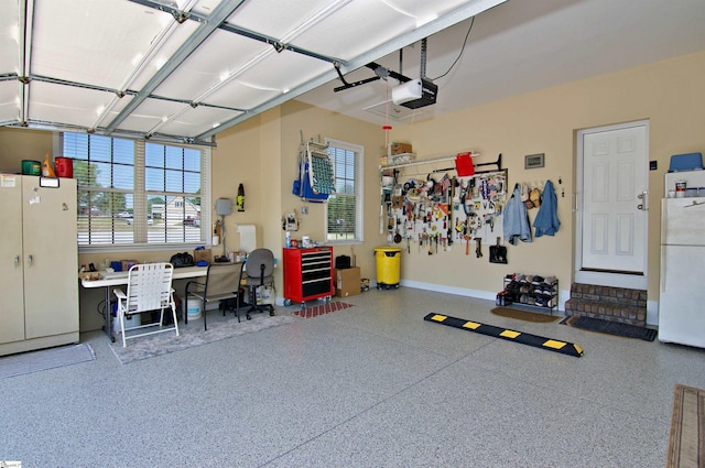 garage with a garage door opener, freestanding refrigerator, and baseboards