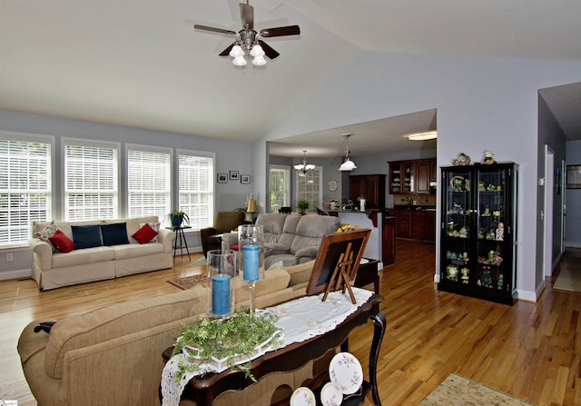 living room featuring light wood-type flooring, ceiling fan with notable chandelier, high vaulted ceiling, and baseboards