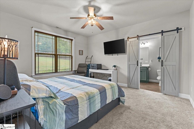 bedroom with baseboards, light carpet, ensuite bathroom, a barn door, and visible vents