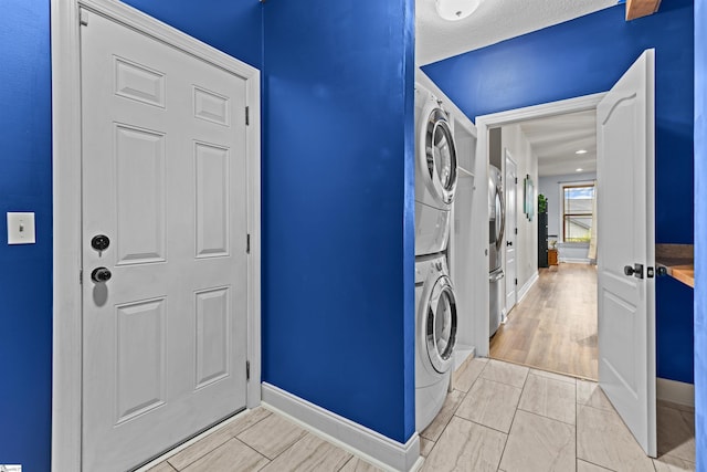 clothes washing area featuring baseboards, stacked washing maching and dryer, and laundry area