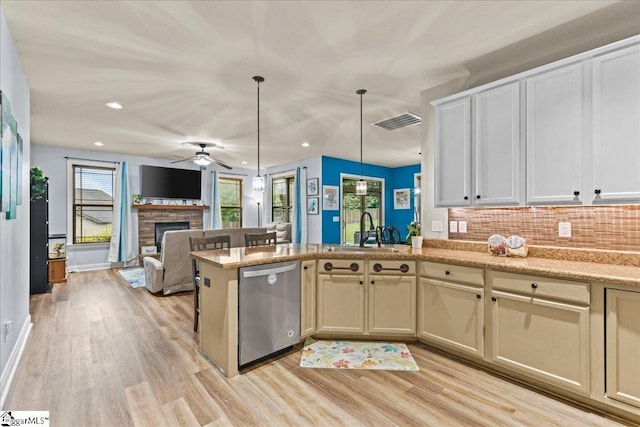 kitchen with stainless steel dishwasher, a fireplace, light wood-style flooring, visible vents, and a sink