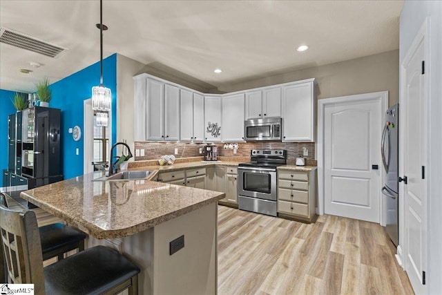 kitchen featuring visible vents, a sink, a peninsula, light wood finished floors, and stainless steel appliances