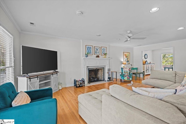 living room featuring ceiling fan, a fireplace with flush hearth, ornamental molding, visible vents, and recessed lighting