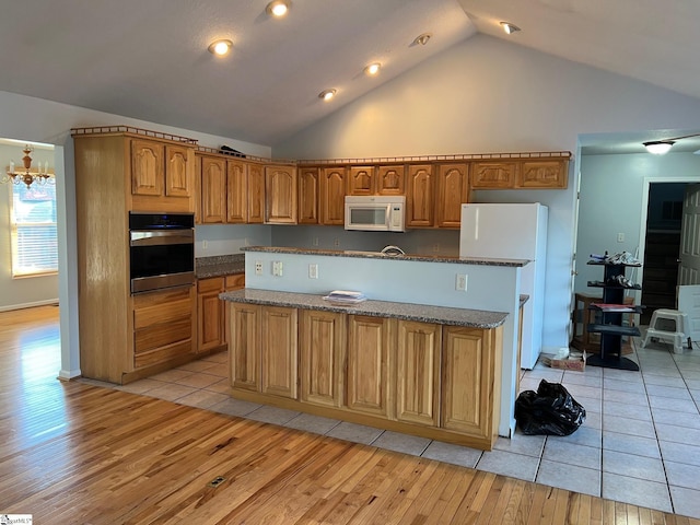 kitchen with light wood-style floors, dark stone counters, white appliances, brown cabinetry, and a kitchen island