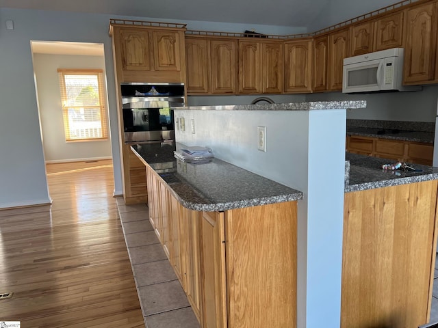 kitchen featuring dark stone counters, white microwave, wood finished floors, and stainless steel oven