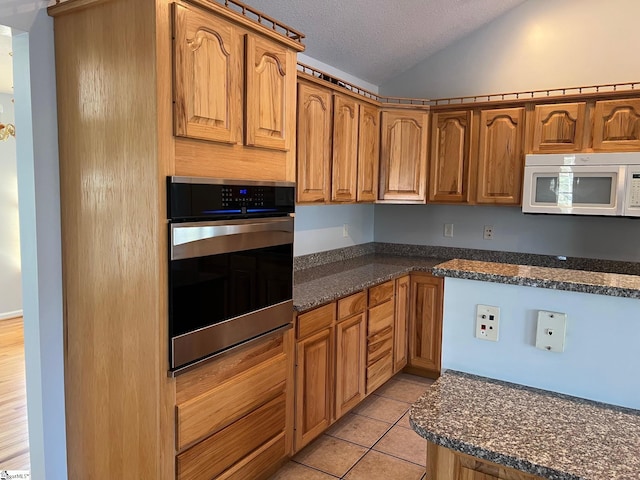kitchen featuring light tile patterned floors, a textured ceiling, white microwave, vaulted ceiling, and stainless steel oven