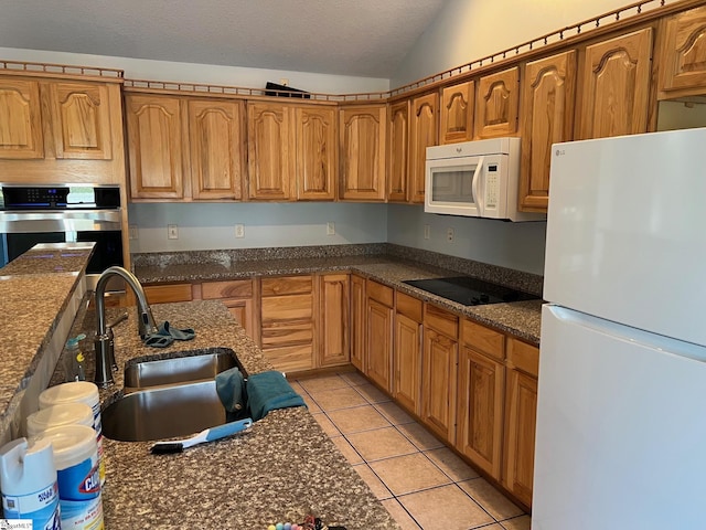 kitchen with light tile patterned floors, white appliances, vaulted ceiling, a sink, and brown cabinets