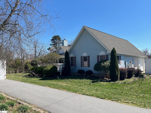 view of side of property featuring an attached garage, a shingled roof, a chimney, and a lawn