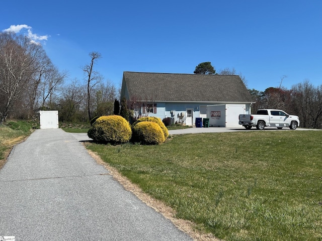 view of side of home featuring a shingled roof, aphalt driveway, and a lawn