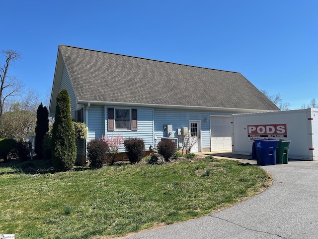 view of front of property featuring roof with shingles, a front lawn, an attached garage, and driveway
