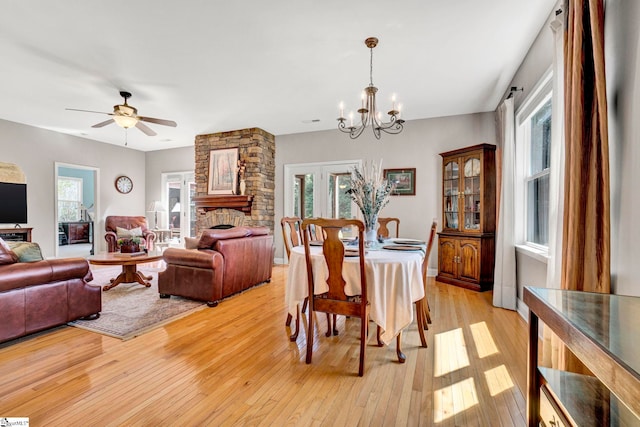 dining space with light wood-type flooring, a healthy amount of sunlight, ceiling fan with notable chandelier, and baseboards