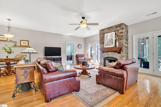 living room with a fireplace, light wood finished floors, visible vents, and a ceiling fan
