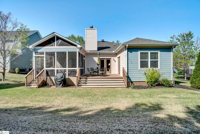 rear view of property with a chimney, a yard, a deck, a sunroom, and a shingled roof