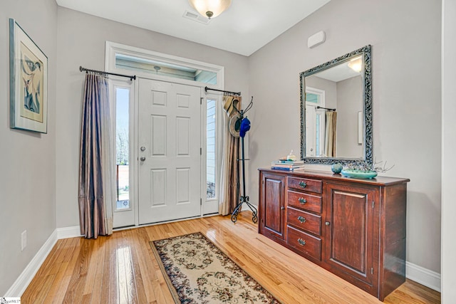 foyer featuring light wood finished floors, baseboards, and visible vents