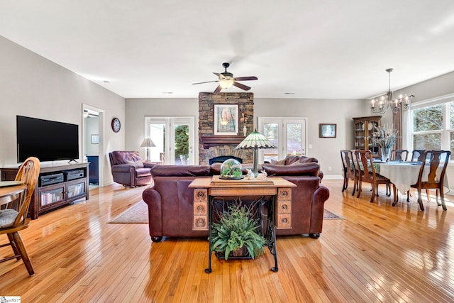 living area featuring light wood-style flooring, ceiling fan with notable chandelier, and a fireplace