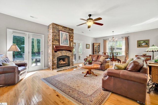 living area with visible vents, a stone fireplace, light wood-type flooring, and ceiling fan with notable chandelier