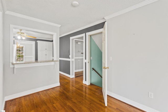 empty room featuring a ceiling fan, wood finished floors, baseboards, and ornamental molding