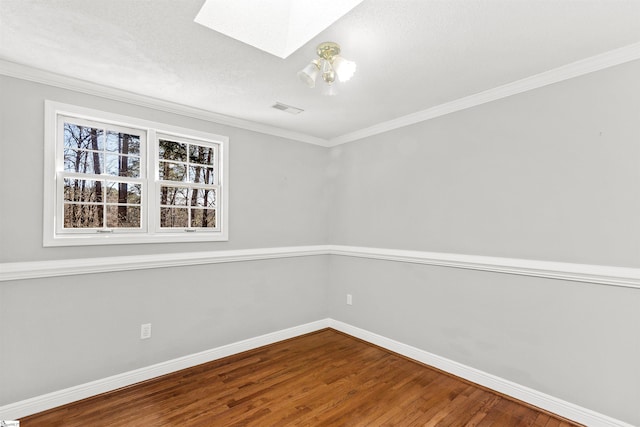empty room featuring ornamental molding, visible vents, a skylight, wood finished floors, and baseboards