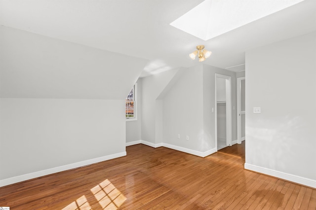 additional living space with vaulted ceiling with skylight, baseboards, and light wood finished floors