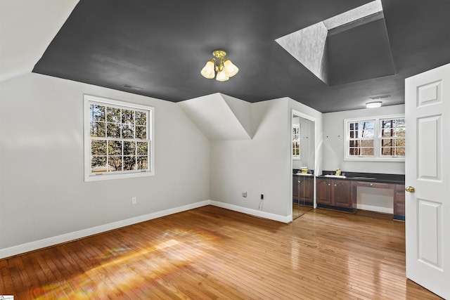 additional living space with light wood-style floors, baseboards, and vaulted ceiling