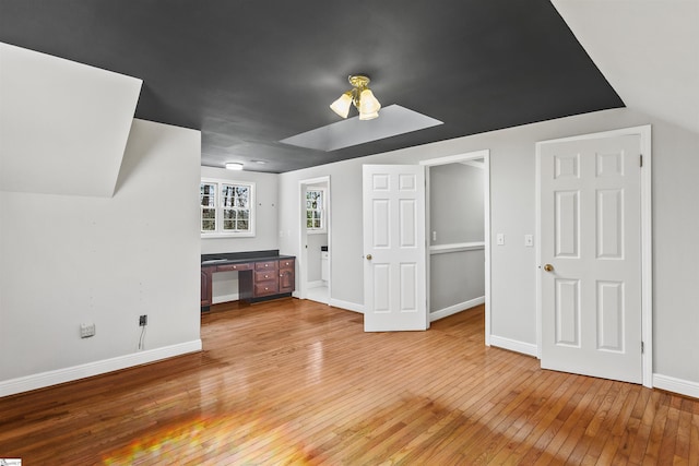 unfurnished living room featuring light wood-style flooring, baseboards, and a skylight