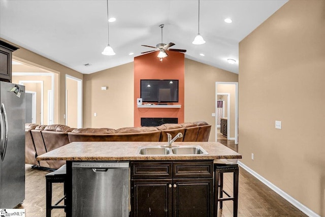 kitchen with a sink, open floor plan, a kitchen bar, dark wood finished floors, and stainless steel appliances
