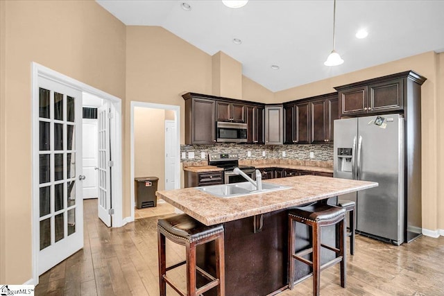 kitchen with a sink, a kitchen breakfast bar, dark brown cabinets, stainless steel appliances, and decorative backsplash