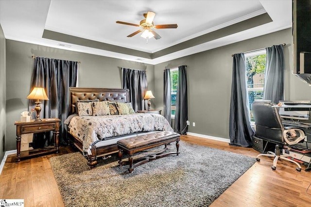 bedroom featuring crown molding, multiple windows, a raised ceiling, and wood-type flooring