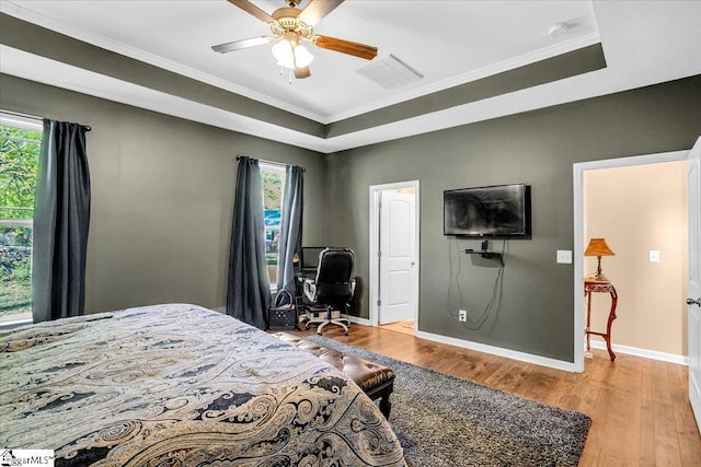 bedroom with multiple windows, a tray ceiling, crown molding, and wood finished floors