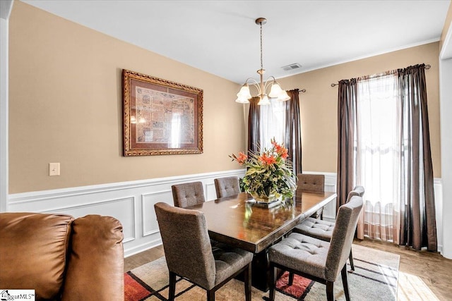 dining space with a chandelier, wood finished floors, visible vents, and a wainscoted wall
