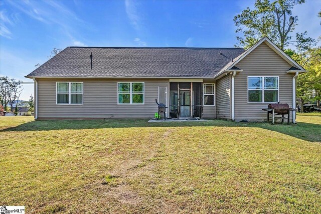 back of property with a shingled roof, a sunroom, and a lawn