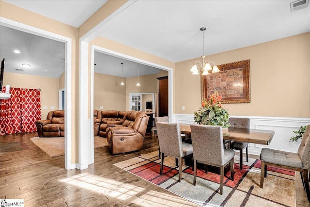 dining space with a notable chandelier, visible vents, a wainscoted wall, and wood finished floors