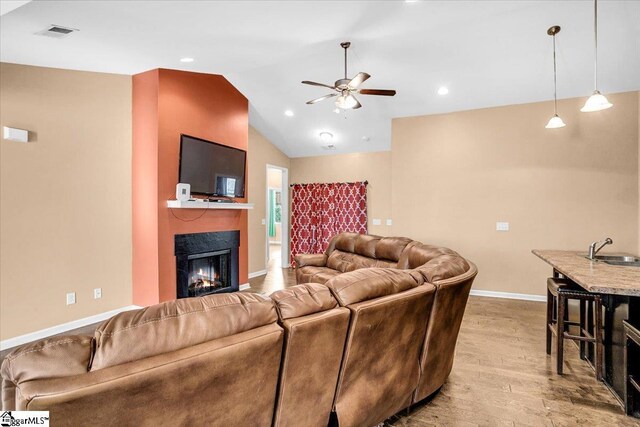 living area with ceiling fan, a lit fireplace, visible vents, wood finished floors, and baseboards