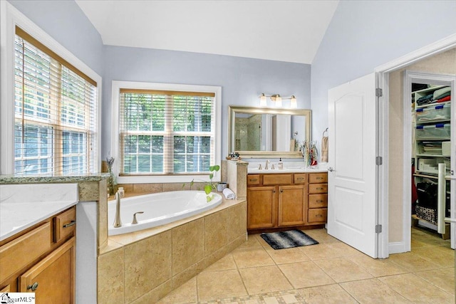 bathroom featuring vanity, vaulted ceiling, tile patterned flooring, a walk in closet, and a garden tub