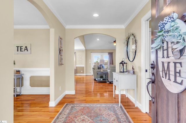 foyer featuring arched walkways, ceiling fan, light wood finished floors, crown molding, and baseboards